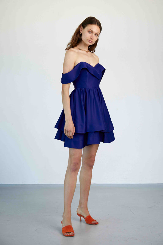 Model trägt das kurze Linda Kleid in königsblau mit Carmen-Ärmeln, Corsage und doppellagigen A-Linien-Rock