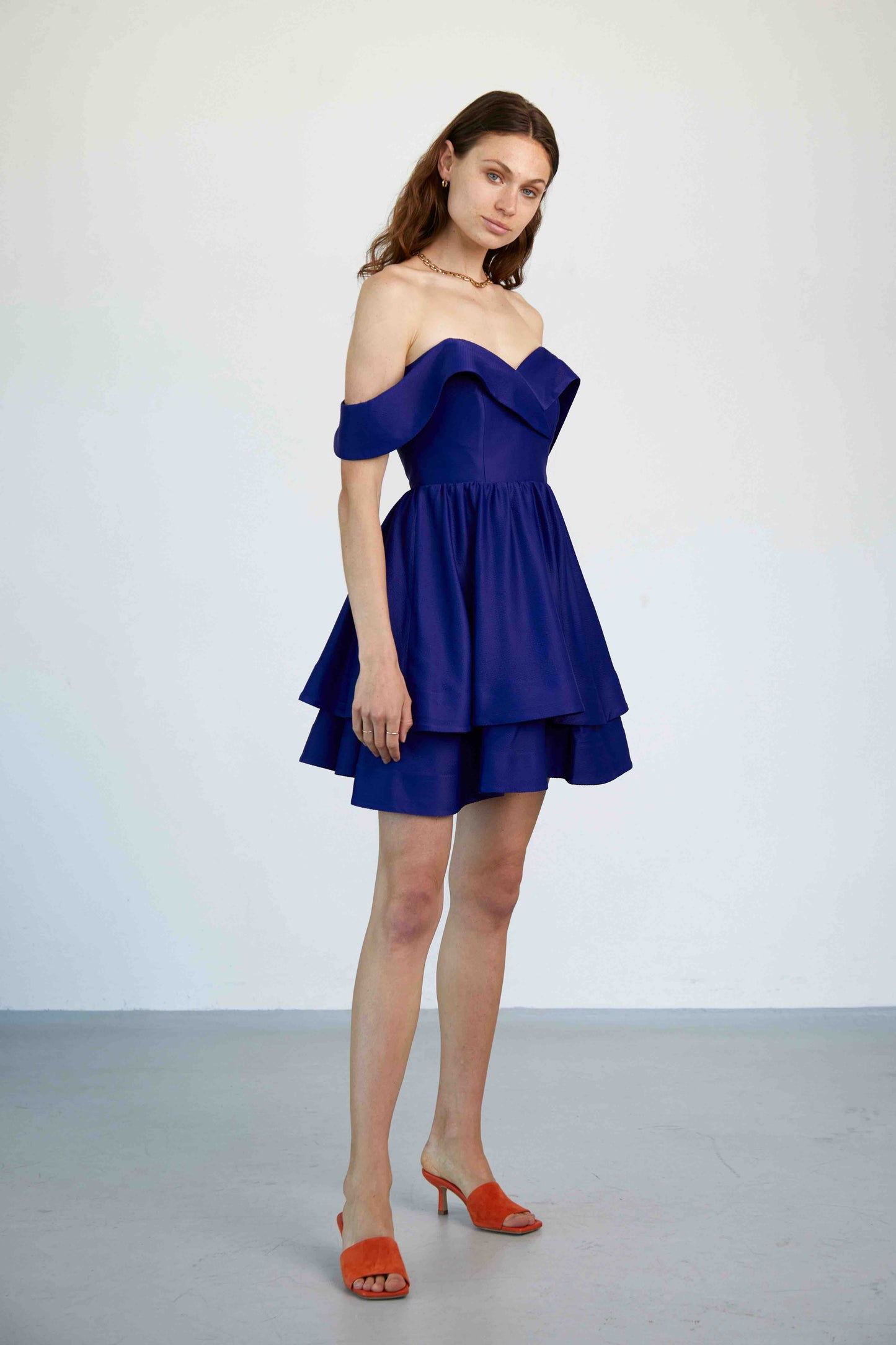 Model trägt das kurze Linda Kleid in königsblau mit Carmen-Ärmeln, Corsage und doppellagigen A-Linien-Rock