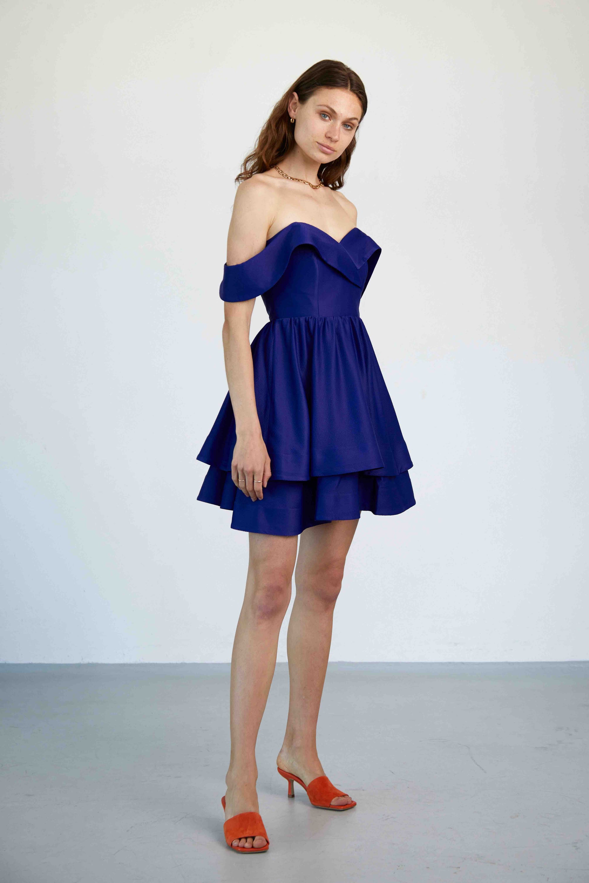 Model trägt das kurze Linda Kleid in königsblau mit Carmen-Ärmeln, Corsage und doppellagigen A-Linien-Rock